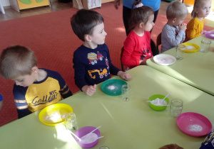 Dzieci siedzą przy stoliczkach i kolorowych talerzykach z solą